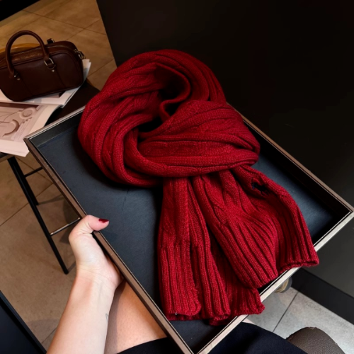 Red scarf in a black box held by a hand on a wooden floor.