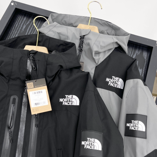 Two hooded outdoor jackets in black and grey hanging on hangers