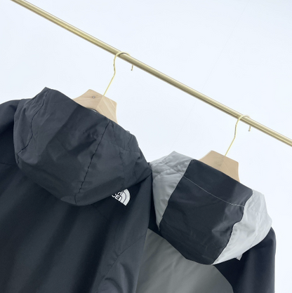 Two hooded outdoor jackets in black and grey hanging on wooden hangers against a white background.